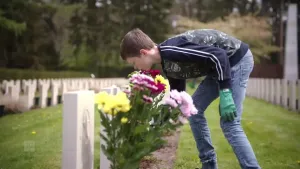 Een foto van een jongen van een jaar of vijftien op een militaire begraafplaats. Hij heeft tuinhandschoenen aan en verzorgt de planten bij de graven. 