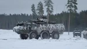 Een foto van een legervoertuig in de sneeuw. Hij staat in een open stuk van een bos. Je ziet het hoofd van een militair uit het voertuig steken. Op de achtergrond staan nog twee legervoertuigen.