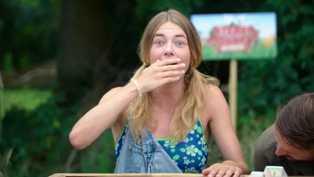 Een foto van Emma die achter een bak staat. Ze heeft een hand op die bak en een hand voor haar open mond. Ze kijkt geschrokken.