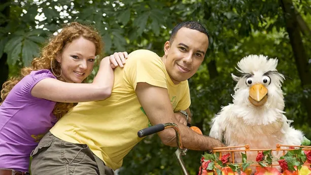 Een foto van de twee presentatoren op een fiets en de vogelpop in de fietsmand voorop.