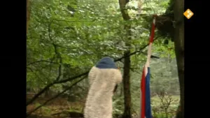 Een foto van Arie in het bos. Op de achtergrond zie je de Nederlandse vlag op een stok in de grond staan. 