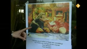 Een foto van een poster op een raam. Op de poster zie je Moffel en Piertje in hun voorstelling. Er staat ook nog wat tekst op de poster. Een hand van een persoon wijst naar deze poster.