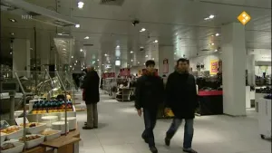 Een foto van de binnenkant van een grote winkel. Daarin staan enkele mensen. Een man staat er stil en twee mensen lopen er.