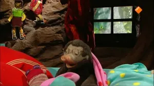 Een foto van Moffel en Piertje in hun huis. Piertje ligt in bed en Moffel staat naast haar bed. Ze kijken elkaar aan. 