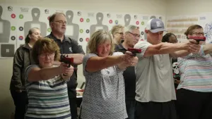 Een foto van leraren van een Amerikaanse school die leskrijgen in het schieten met een wapen. De vier leraren vooraan richten een  pistool op een op de foto niet zichtbaar doel. Aan de muur erachter hangen enkele doelen met de vorm van een mens erop.