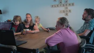 Een foto van Igor die met zijn gezin aan een tafel zit. Ze kijken allemaal naar een laptop die vooraan op de tafel staat. Igor zit in een rolstoel, omdat hij de spierziekte A L S heeft. Het gezin bestaat uit zijn vrouw en drie kinderen. 