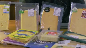 Een foto van tien pakjes van doorzichtig plastic op een tafel. In elk daarvan zitten plakken kaas. Sommige pakjes liggen op de tafel en andere staan rechtop.