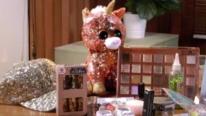 Een foto van een tafel met daarop spullen met glitter erop. Je ziet een petje met glitter, een knuffel met glitter, en glitter make-up.