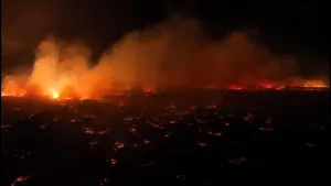 Een foto van een natuurbrand, waarop de door brand rood oplichtende omgeving en van de omgeving opstijgende rookwolken zichtbaar zijn. Doordat de foto in het donker genomen is, is op de foto niet goed zichtbaar wat er in de brand staat.
