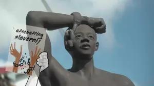 Een foto van een beeld van een man met een arm op zijn hoofd. Aan de arm hangt een ketting met één gebroken metalen ring. Links voor de man staat een getekend plaatje met de tekst "afschaffing slavernij" en twee armen aan een metalen ketting die breekt.