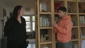 Een foto van presentator Nizar die in de huiskamer met een vrouw aan het praten is. Naast hun staat een kast waar ook boeken in zitten.