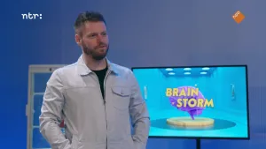 Een foto van een man, met rechts achter hem een groot televisiescherm. Hierop is de naam "Brainstorm" te zien, en het logo van het programma: een animatie van een stel hersenen boven een ronde schijf. Links achter hem staat een kast. 