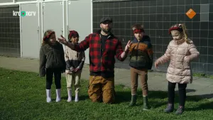 Een foto van boswachter Tim die op zijn knieën zit in het gras tussen vier kinderen die naast hem staan.