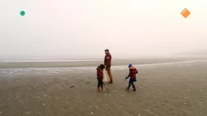 Een foto van boswachter Tim en twee kinderen op het strand. Tim heeft een zak in zijn hand. De kinderen hebben allebei een stok in hun handen om voorwerpen op te kunnen rapen van de grond. Op de achtergrond is een stukje zee te zien.