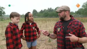Een foto van boswachter Tim en twee kinderen. Tim staat op zijn knieën, zodat hij even groot is als de anderen. Ze praten met elkaar. Ze staan in een zanderig gebied met weinig planten. Op achtergrond zijn bomen te zien.