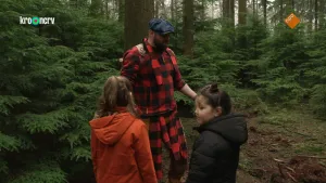 Een foto van boswachter Tim en twee kinderen in een bos. Een kind kijkt om zich heen en de ander kijkt naar Tim. 