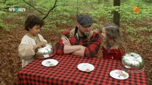 Een foto van boswachter Tim met twee kinderen aan een tafel. Op de tafel liggen drie bordjes met daarop papiertjes. Er zijn ook twee metalen halve bollen waarmee de bordjes bedekt kunnen worden. Tim praat met een kind, de ander houdt zo'n halve bol vast.