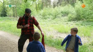 Een foto van boswachter Tim met twee kinderen op een pad in een bosachtig gebied. De kinderen kijken naar Tim, en een rent weg. Tim staat alsof hij zich gaat verdedigen.