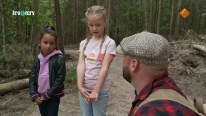 Een foto van boswachter Tim en twee kinderen die in een open plek in een bos staan. Tim staat dichter bij de camera en praat met de kinderen. 