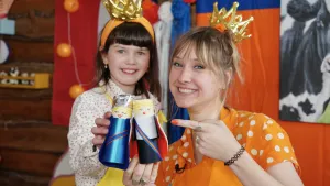 Een foto van Rosalie en Sophie. Rosalie heeft een geknutselde Willem-Alexander vast, die een zwart pak met witte blouse draagt en een mantel erover. Sophie heeft de geknutselde koningin Máxima vast, die een blauwe jurk draagt en een zilverkleurige kroon. 
