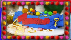 Een foto van een geknutselde snoepjesdoos in lichtblauw crêpepapier. Er zitten twee goudkleurige strikken aan allebei de kanten. Er liggen knutselbolletjes op en goudkleurige glitters. Op de voorkant staat "Eid Mubarak", wat "Gezegend Feest" betekend.