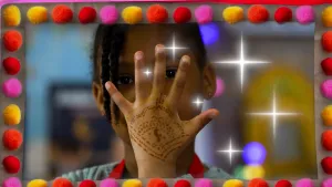 Een foto van Djahmiyah die de buitenkant van haar hand voor de camera houdt. Op de hand zit een getekende hennah versiering met allemaal kleine stipjes en streepjes die stippellijntjes en cirkels vormen in een donkerbruine kleur.