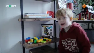 Een foto van Jesse, een jongen in een rode trui met capuchon die naar de camera kijkt. Achter Jesse staat een speelgoedboerderij en zijn planken te zien met vier boeken erop, Duplo bouwstenen en een omgedraaide doos met microscoop erin.