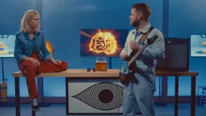 Een foto van presentator Janouk in de studio van Brainstorm. Naast haar staat een gitarist. Ze kijken elkaar aan. 