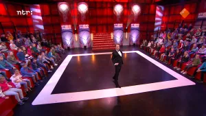 Foto van de studio van Snugger waarbij de presentator op het podium staat, links en rechts ervan zit het publiek.