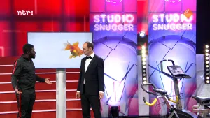 Foto van de studio van Snugger waarbij de presentator op het podium staat met een andere man, op een groot beeldscherm is een goudvis te zien.