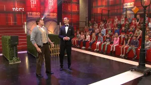 Foto van de studio van Snugger, publiek is te zien, op het podium staat de presentator en bij hem staat een andere man.