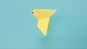 Foto van een eenvoudig geel vogeltje gevouwen van papier, op de kop een oogje geplakt.