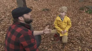 Een foto van boswachter Tim in het bos. Op de grond liggen veel herfstbladeren. Voor Tim zit een jongetje. Tim legt iets uit aan dat jongetje. 