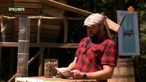 Een foto van boswachter Tim. Hij staat buiten en leest iets voor vanaf een blaadje. Hij heeft een rood-zwart geruit overhemd aan en een pet op. Op de achtergrond zie je een boomhut en een bord met daarop de foto van een wild zwijn.