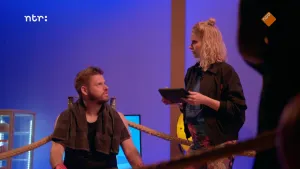 Een foto van presentator Job die in de hoek zit van een boksring met een handdoek over zijn schouders. Presentator Janouk staat naast hem buiten de ring.