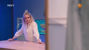 Een foto van presentator Janouk die met haar handen leunt op een tafel die voor haar staat in de Brainstorm studio.