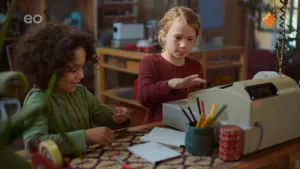 Een foto van Saïd en Anna die achter een balie met een kassa erop staan. Saïd staat links en kijkt naar de geldmunt in zijn hand. Recht staat Anna achter de kassa en is met haar rechterwijsvinger met aandacht bezig een getal in te toetsen op de kassa.