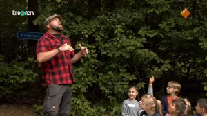 Een foto van Boswachter Tim in een zwartrood geruite blouse en bruin gestipte pet op voor een groep zittende kinderen. Tim heeft zijn ogen dicht en zijn hoofd in de lucht tijdens het zeggen van "heel" in over welk dier ze het heel graag willen hebben.