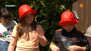 Een foto van een jongen en een meisje met een rode hoed op en een ander kind dat wacht erachter. Het meisje draagt een oranje t-shirt en de jongen een zwart t-shirt van de voetbalclub Ajax. Rechts is de wit met bruine pet van Boswachter Tim te zien.