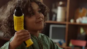 Een foto van Saïd die omhoogkijkt naar rechts en in zijn linkerhand een gele schroefmachine met een zwarte kop in de lucht steekt. Een schroefmachine is een elektrisch stuk gereedschap om schroeven mee vast te kunnen draaien.