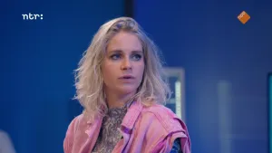 Een foto van Janouk die naar rechts kijkt naar prof, die niet in beeld is. Janouk heeft een roze jasje van spijkerstof aan over een grijze blouse met gekrulde vormen erop.