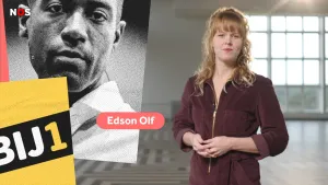 Een foto van een presentator in een lege kamer met links een foto van de lijsttrekker van de politieke partij Bij1 en zijn naam: Edson Olf. De partijnaam Bij1 staat voor de foto van Edson in witte letters op een zwarte strook met een gele achtergrond.