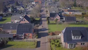 Een foto, vanuit de lucht genomen, van twee rijen vrijstaande huizen tussen een weg. De twee voorste huizen hebben zonnepanelen op het dak. Bij de huizen liggen ook grasvelden en er staan enkele bomen en struiken op de grond bij de huizen.