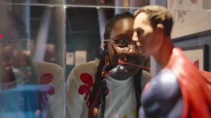 Een foto van presentator Tirsa die naar een Superman pop kijkt die in een bak staat waar je doorheen kan kijken.