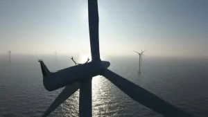 Een foto van een windmolen op zee van dichtbij genomen. Op de achtergrond zijn er nog meer zee windmolens te zien.