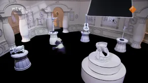 Een foto van een museum met vijf witte objecten op vijf witte tafels. Het zijn een betonwagen, een hijskraan, een akoestische gitaar, een stoplicht en een vaas waar bijna de helft vanaf gebroken is. Een pop met paarse vacht rent tussen twee tafels door.