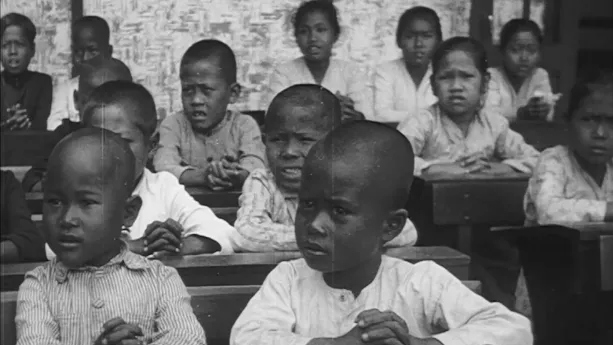 Een foto in zwart-wit met veel kinderen die in de klas zitten.