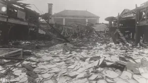 Een foto in zwart-wit van de ruïnes van een gebouw waar door het verzet een aanslag op was gedaan. Er zijn op de grond nog veel papieren te zien.