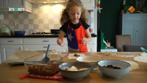 Een foto van een meisje in een schort met daarop de Chileense vlag, die achter een tafel staat. Ze gaat empanadas maken, een snack uit Chili van bladerdeeg gevuld met ingrediënten die voor het meisje in kommen staan: vlees, olijven, ei en rozijnen.