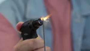 Een foto van de hand van de presentator die een kleine gasbrander vastheeft en daarmee een sterretje aansteekt. Een sterretje is een staafje brandbaar vuurwerk dat vonkjes afgeeft in de vorm van sterretjes. 